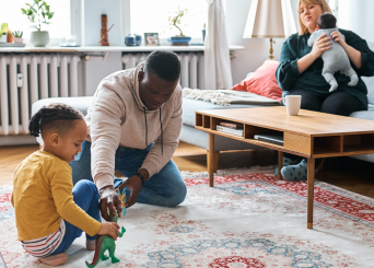 Papa qui joue avec son enfant pendant que maman s’occupe du bébé.