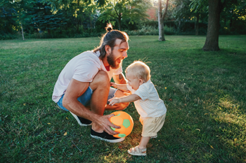 A dad playing ball outside with his baby